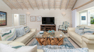 Glass coffee table on a gnarled root base and a floral carved armchair in the TV lounge at Queens Fort Pavilion, Barbados