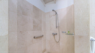 Beige-tiled open walk-in shower with a handheld shower head on a rail and a grab bar at Queens Fort Pavilion, Barbados