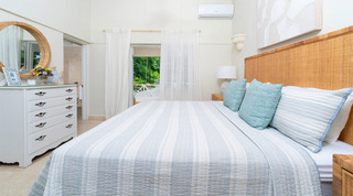 Woven rattan headboard and round mirror in a bedroom with a door open to a garden veranda at Queens Fort Pavilion, Barbados