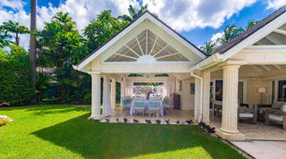 Dining pavilion behind a white sunburst gable and fluted columns, seen from the lawn at Queens Fort Pavilion, Barbados