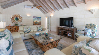 Cream leather sofas and a floral carved armchair beside the television in the lounge at Queens Fort Pavilion villa, Barbados