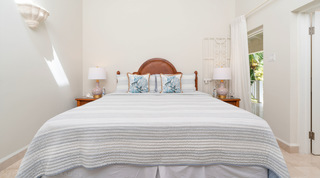 Arched cane headboard between pink floral porcelain lamps, a door open to the veranda, at Queens Fort Pavilion, Barbados