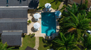 Aerial view looking down on the pool, white parasols and shingled roofs of Queens Fort Pavilion, private villa in Barbados