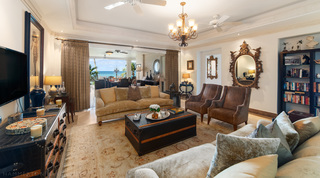 Bookcase, ornate gold oval mirror and brown armchairs in Smugglers Cove 3's living room, holiday apartment in Barbados