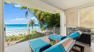Sun loungers and a barbecue on the covered terrace above the beach at Smugglers Cove 3, beach apartment in Barbados