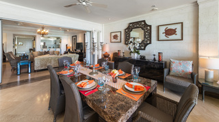 Dining table with orange napkins by open doors to the chandelier-lit living room, Smugglers Cove 3 apartment rental, Barbados