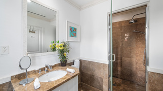 Vanity with orchids and a koi painting beside a glass-door shower at Smugglers Cove 3, luxury apartment in Barbados