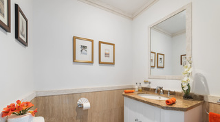 Guest cloakroom with orange hand towels, a white orchid in a tall vase and gold-framed prints at Smugglers Cove 3, Barbados