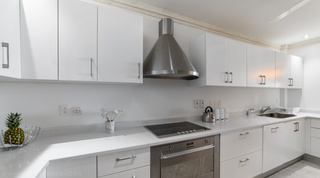 White gloss kitchen with a steel cone extractor, hob and built-in oven at Smugglers Cove 3, a Barbados apartment rental