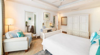 Armchair with coral-motif cushion, dressing table and cream armoire beside the en-suite, Smugglers Cove 3 in Barbados