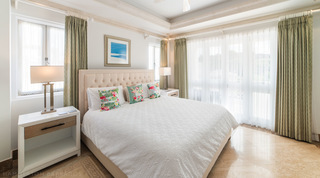 King bed with buttoned headboard and flamingo cushions by sheer-curtained windows, Smugglers Cove 3 apartment in Barbados