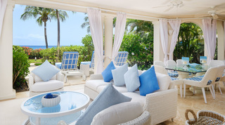 Shaded terrace with white wicker sofas and the sea beyond the palms at St. Peter's Bay 104, luxury apartment in Barbados