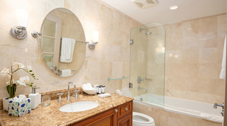Shower over the bath behind a glass screen, with a single vanity and oval mirror, at St. Peter's Bay 104, Barbados