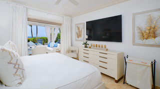 Chest of drawers, wall TV and gold palm-frond art in the main bedroom at St. Peter's Bay 104 in Barbados