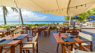 Wooden tables laid with folded napkins on the beachside restaurant deck shared by St. Peter's Bay 106 guests, Barbados