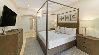 Four-poster bed and a wall-mounted TV above a wooden chest of drawers in a St. Peter's Bay 106 bedroom, Barbados