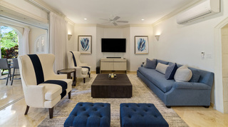 Wall-mounted TV between blue frond prints, with a long blue sofa to one side, at St. Peter's Bay 106, Barbados