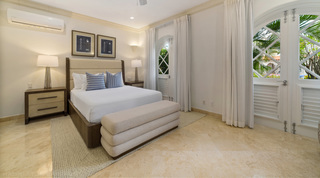 Upholstered headboard and lighthouse blueprint prints by arched glazed doors in a St. Peter's Bay 106 bedroom, Barbados