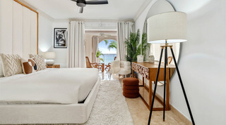 Wood-block console, tripod lamp and rust pouf in a sea-facing bedroom at St. Peter's Bay 204, Barbados