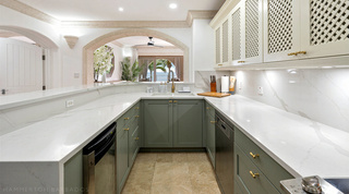 Sage-green kitchen with brass handles and white veined worktops, sea beyond, at St. Peter's Bay 204, Barbados