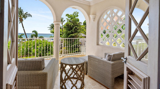 Arched balcony at St. Peter's Bay 204 with grey woven seating, a carved side table and the sea through an arch, Barbados