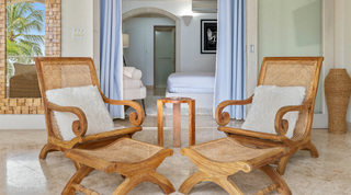 Two planter's chairs with fluffy cushions before a bedroom doorway framed by blue curtains, St. Peter's Bay 204 in Barbados