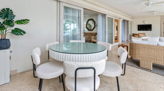 Round dining table with white upholstered chairs by open sliding doors at St. Peter's Bay 204, a Barbados holiday apartment
