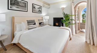Light wood bed beneath framed beach and palm prints, balcony door beyond, in a St. Peter's Bay 204 bedroom, Barbados