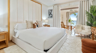 Bedroom with a tall upholstered headboard opening to a sea-view terrace, St. Peter's Bay 204 holiday apartment, Barbados