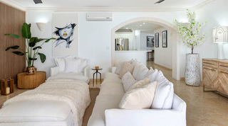 White living room with portrait artwork and an arch through to the kitchen at St. Peter's Bay 204, on Barbados' west coast