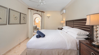 Bedroom with a slatted dark wood headboard and framed seashell prints in St. Peter's Bay 207 apartment, Barbados