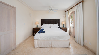 St. Peter's Bay 207 bedroom with a panelled dark wood headboard and an arched lattice door to the balcony, Barbados