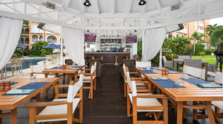 Curtained poolside bar pavilion with wooden tables and director's chairs at the St. Peter's Bay 207 resort, Barbados