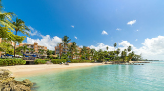 Rock-edged turquoise bay and pale beach, the apricot resort behind, home to St. Peter's Bay 308, luxury apartment in Barbados