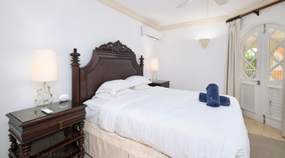 Glass lamps flank a bed with a carved crest and woven headboard, St. Peter's Bay 308 apartment rental, Barbados