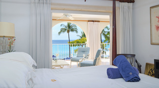 Rolled blue towels on the bed, with terrace armchairs and sea through a curtained opening, St. Peter's Bay 308 in Barbados