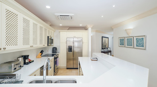 At St. Peter's Bay 308 in Barbados, a double sink and lattice cupboards, with teal geometric prints in the hall beyond