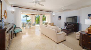 At St. Peter's Bay 308 in Barbados, a cream sofa and armchairs, a TV on a dark wood unit and sea through the arches beyond