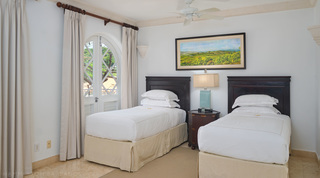 Twin beds with dark headboards under a painting of green hills and coast, St. Peter's Bay 308 holiday apartment, Barbados