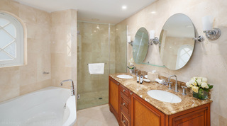 Caramel-toned vanity with white roses, glass shower and bath below an arched window, St. Peter's Bay 308, Barbados