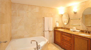 Bath with deck-mounted taps beside the twin-basin vanity in the cream-tiled bathroom of St. Peter's Bay 401 in Barbados