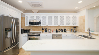 Stainless fridge freezer and a microwave over the cooker in the lattice-cupboard kitchen at St. Peter's Bay 401 in Barbados