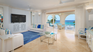 At St. Peter's Bay 401, Barbados, white seating and a blue rug fill the living room, curtains drawn back to the terrace