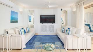 Facing white sofas with striped cushions around a blue rug, a TV between tall mirrors, St. Peter's Bay 401, Barbados