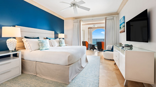 St. Peter's Bay 404 bedroom with a deep blue feature wall, opening through curtains to the sea-view terrace, Barbados