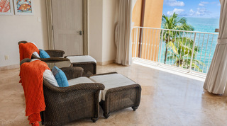 Two woven armchairs with footstools and orange throws facing the sea on the terrace of St. Peter's Bay 404, Barbados