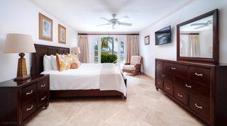 Bedroom at Sugar Cane Ridge 2 – Coral Blu, Barbados, with a dark wood bed and arched French doors open to a flowering hedge