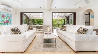 Tree House Villa 5's twin white sofas flank the coffee table, folding doors open beyond, Barbados