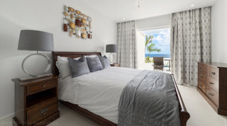 Dark wood bedroom at Westmoreland Hills 25 with metal wall art and a glimpse of the sea, Barbados